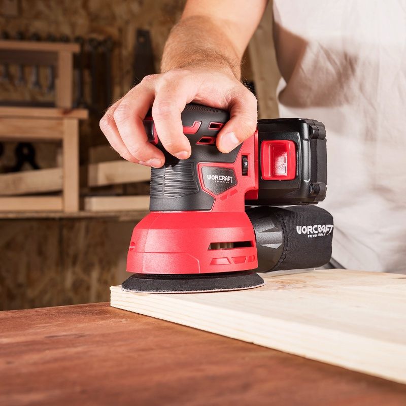 Людина шліфує край дерев’яної панелі за допомогою акумуляторної ексцентрикової шліфмашини WORCRAFT CRS-S20Li.
