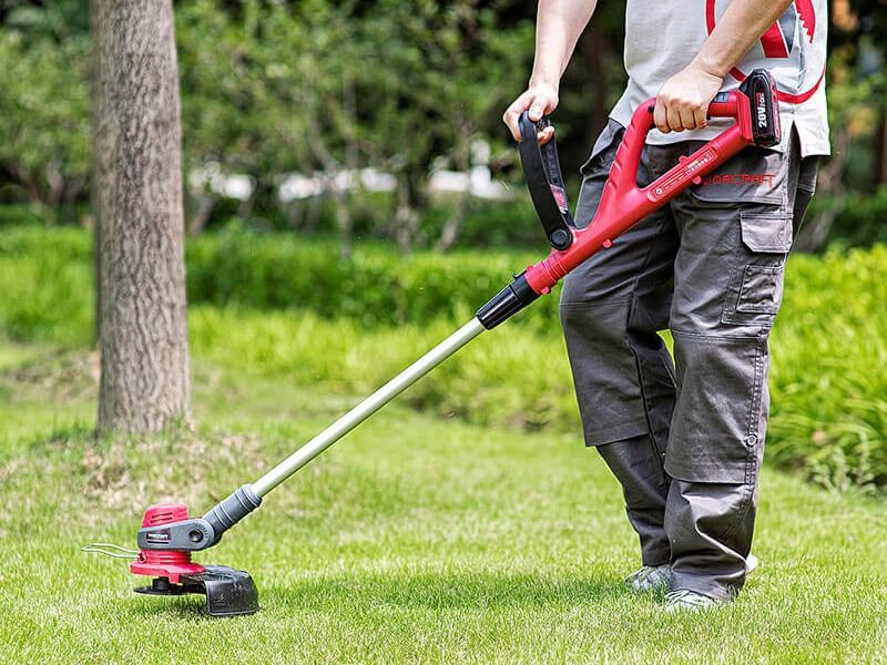 Мужчина косит траву аккумуляторным триммером WORCRAFT CGT-S20LiD на зелёной лужайке.