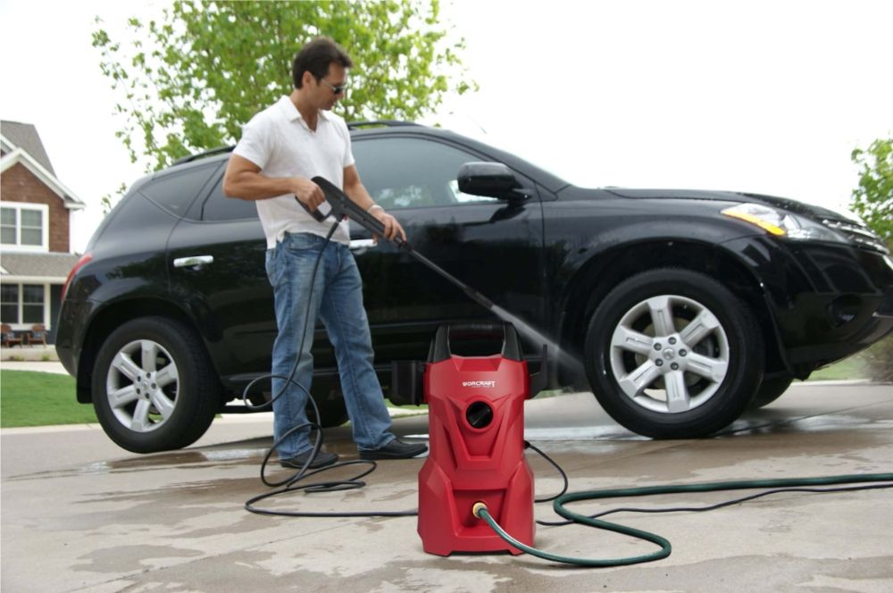Мужчина моет чёрный автомобиль с помощью мойки высокого давления WORCRAFT HC14-070 на подъездной дорожке.