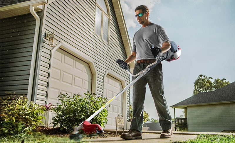 Чоловік працює бензокосою WORCRAFT біля будинку.