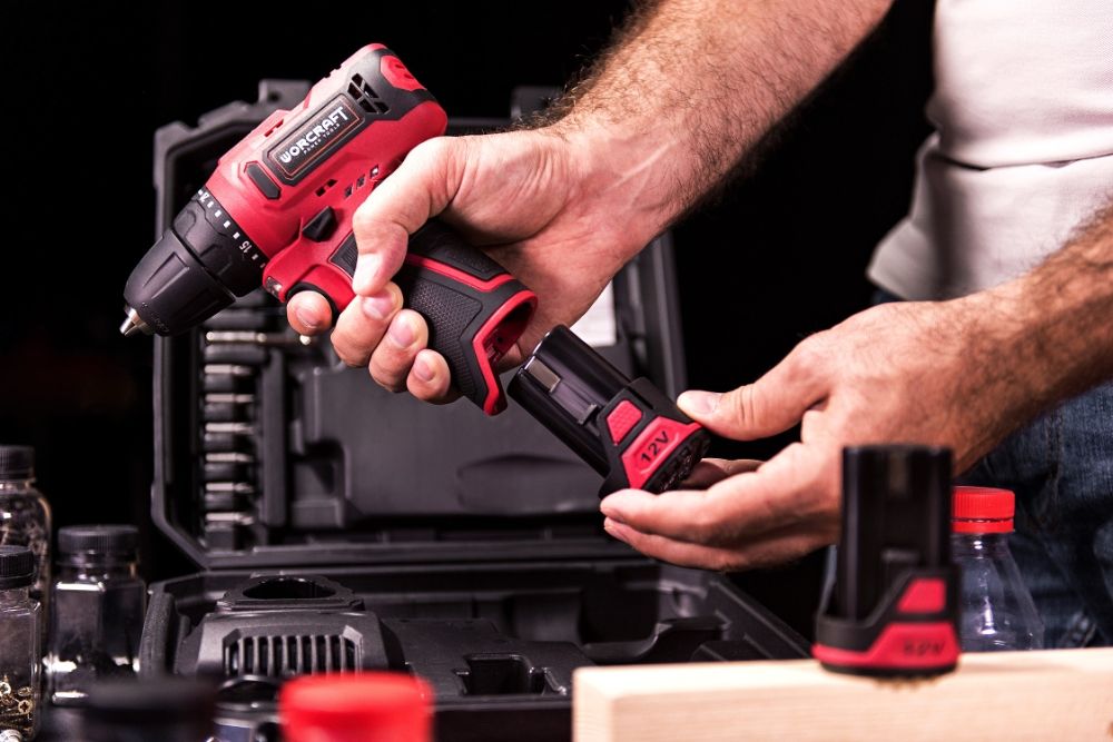 Мужчина меняет аккумулятор на шуруповёрте WORCRAFT CD-12LiA возле кейса с инструментами.