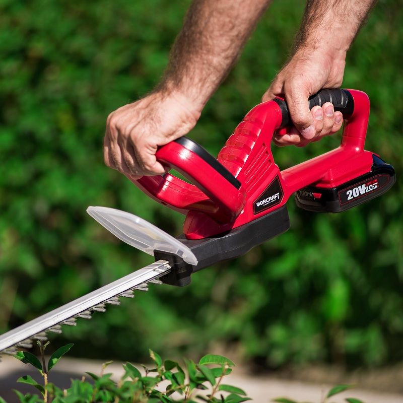 Крупный план работы аккумуляторным кусторезом WORCRAFT по стрижке кустарника.
