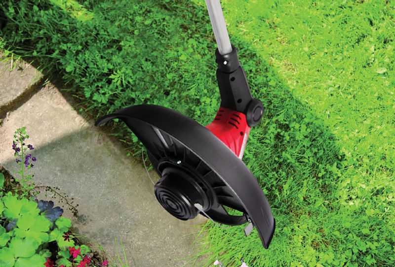 Крупный план режущей головки триммера WORCRAFT EGT07-300 на фоне зелёной травы.