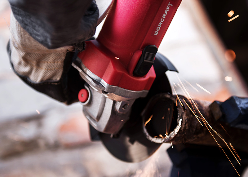 Угловая шлифмашина WORCRAFT активно шлифует металл, вокруг много искр.