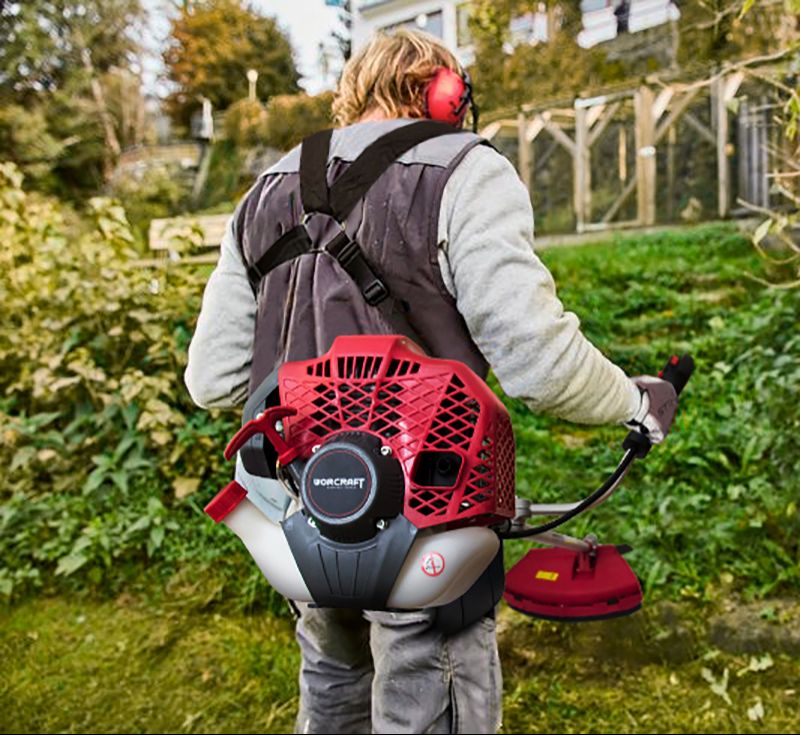 Рабочий несёт мотокосу WORCRAFT WGT52-280 в ранцевом креплении, готовясь к работе.