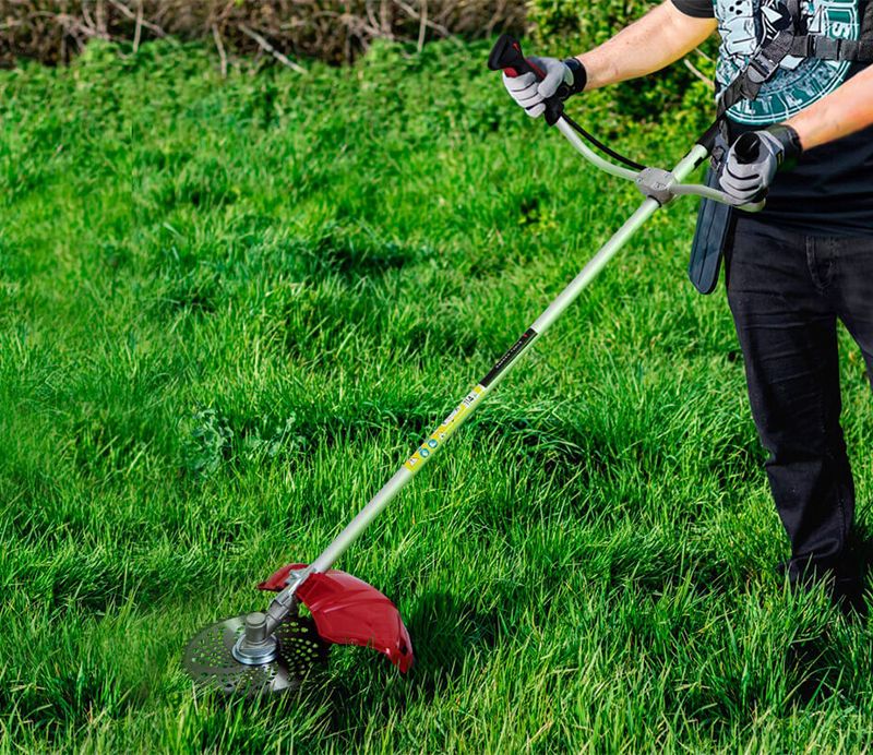 Чоловік косить високу траву бензокосою WORCRAFT.