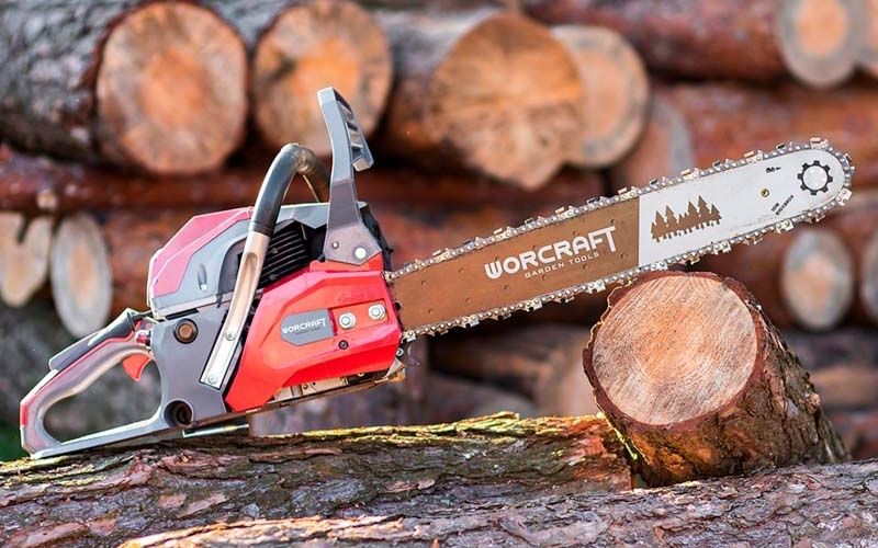 Бензопила WORCRAFT GCS52-20D на фоні дров — вигляд збоку.