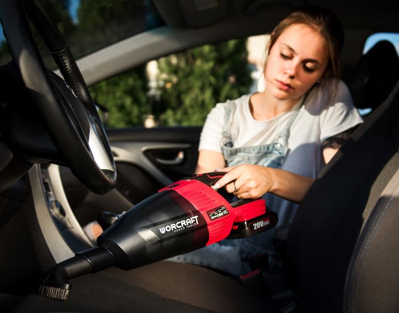 Женщина чистит салон автомобиля ручным аккумуляторным пылесосом WORCRAFT.