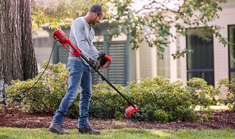 Мужчина использует электрический триммер WORCRAFT EGT19-380 HB для стрижки травы в саду.