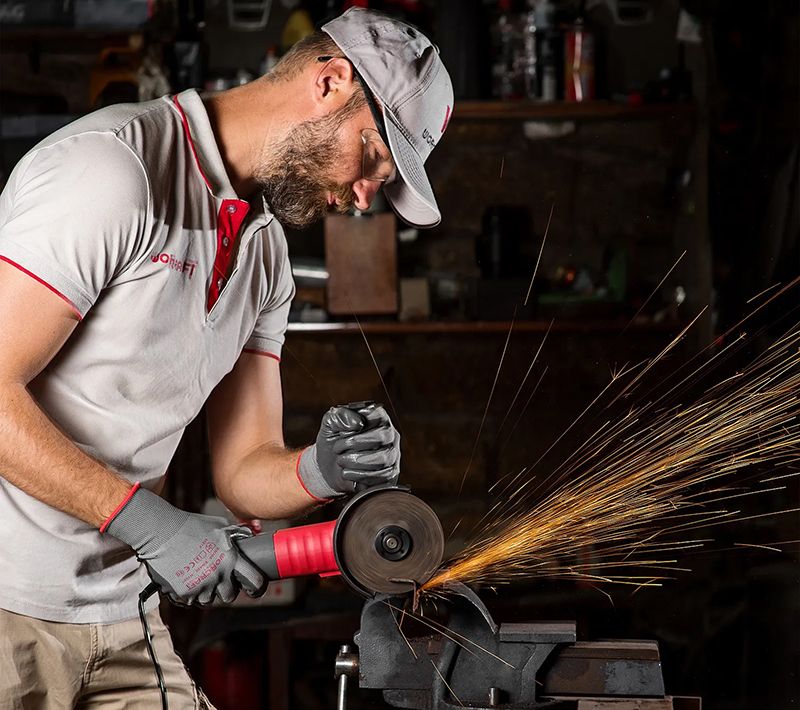 Мужчина в мастерской работает угловой шлифмашиной WORCRAFT AG08-125S — обрабатывает металл с искрами.