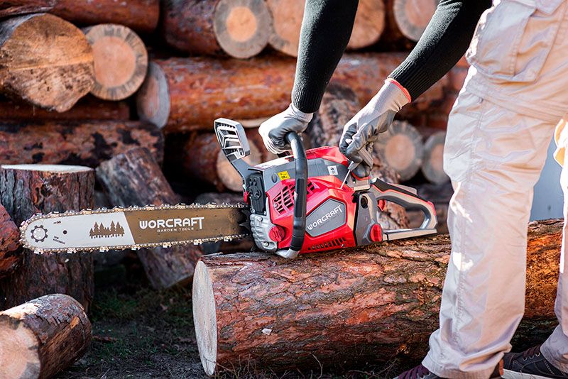 Людина пиляє колоду бензопилою WORCRAFT GCS52-20D на фоні складених дров.
