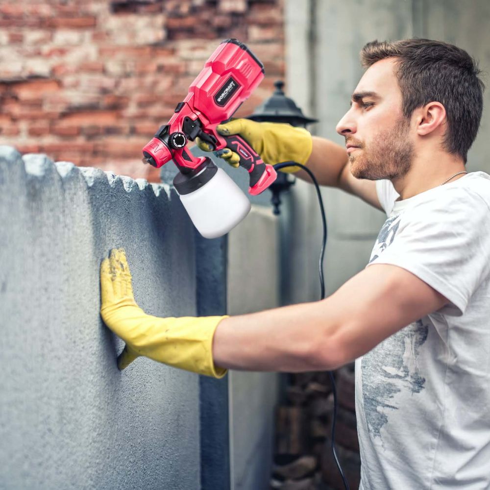 Мужчина использует электрический краскопульт WORCRAFT SG06-800 для покраски металлического забора.