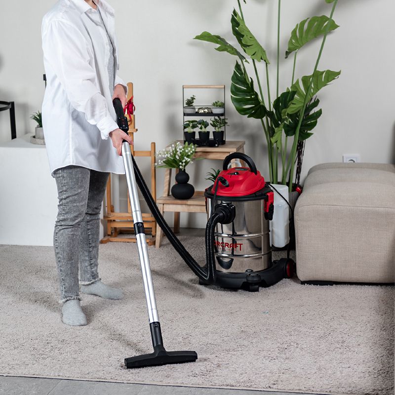 Женщина пылесосит ковер в комнате